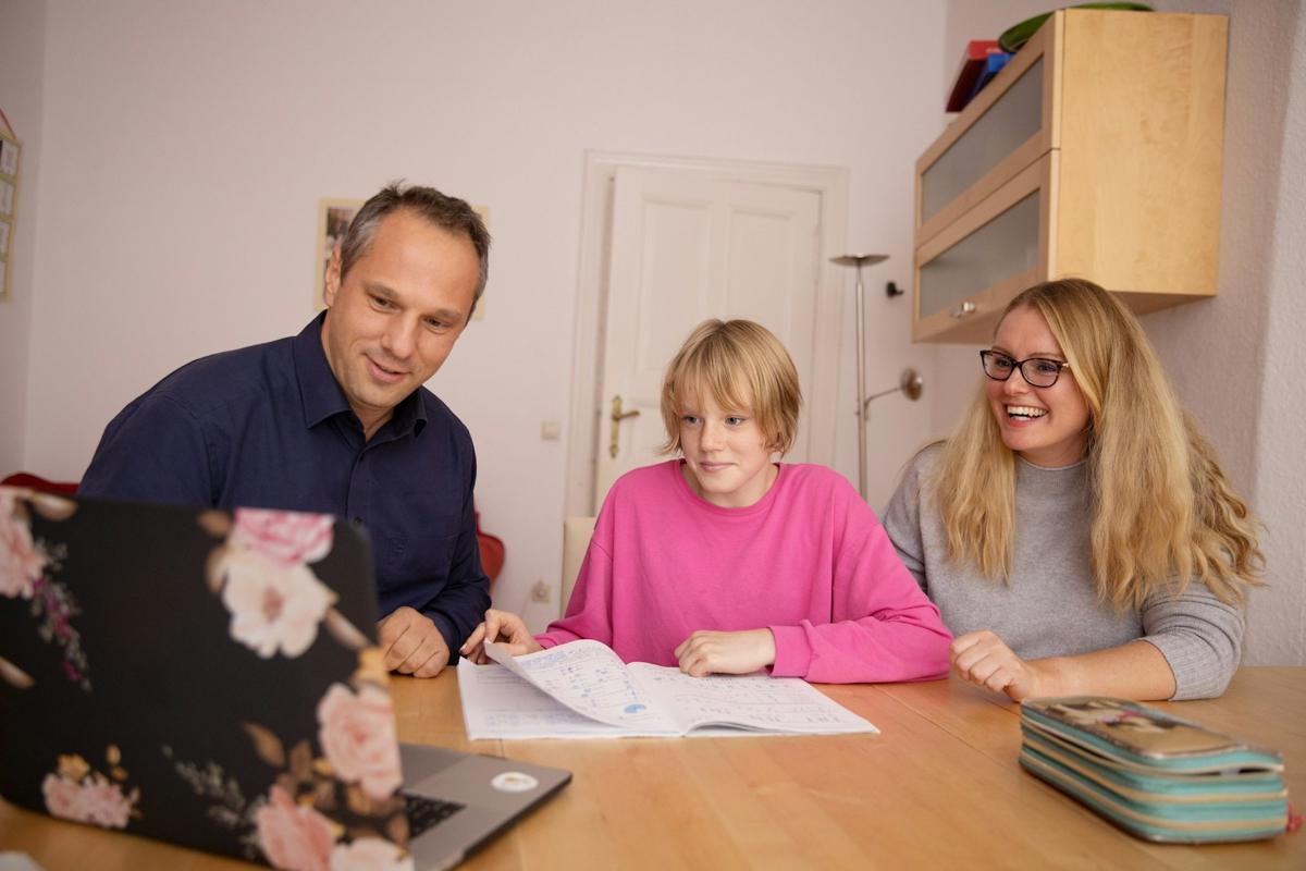 Two parents smiling as they work through homework with their daughter