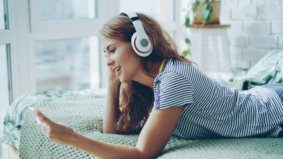 A smiling secondary student in headphones studying from her phone